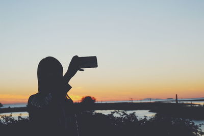 Silhouette of woman holding camera at sunset