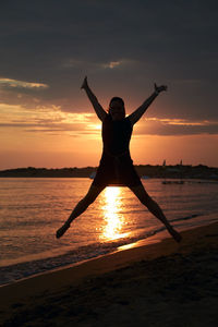 Black silhouette of a woman jumping in the air in the shape of an x. in the background evening sky