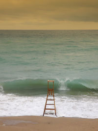 Lifeguard chair on shore at beach during sunset