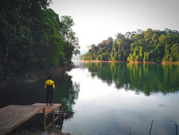 Rear view of man standing by lake against sky