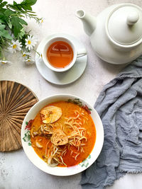 A bowl of curry noodles and a cup of tea with selective focus and blurry background