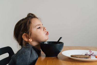 Side view of cute girl eating food at home