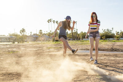 Happy female friends playing in dust on land against clear sky