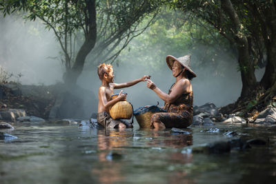 Smiling grandmother and grandson sitting with baskets in river