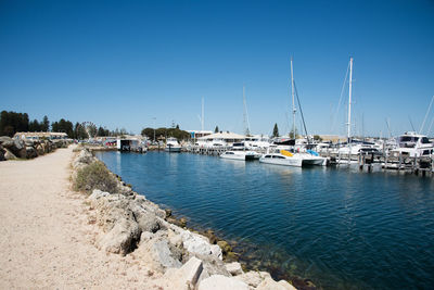 Sailboats moored at harbor against clear blue sky