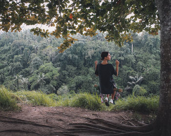 Young woman swinging by tree in forest