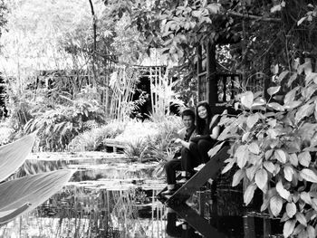 Woman sitting by plants against trees