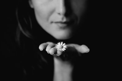 Close-up of hand holding flower over black background