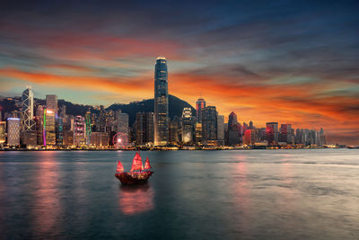 Ship in sea against illuminated building during sunset