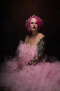 Topless woman wearing tulle skirt sitting against black background