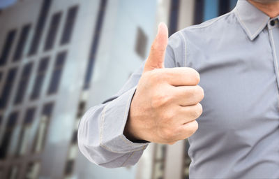 Midsection of businessman gesturing thumbs up in city