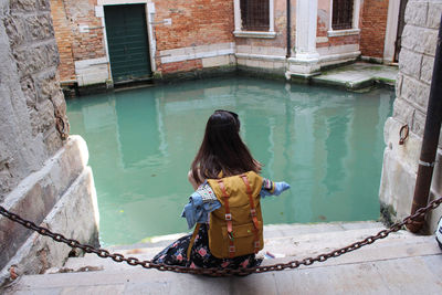 Rear view of woman sitting in canal