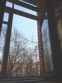 Low angle view of bare trees against sky seen through window