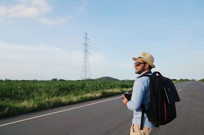 Man using mobile phone while standing on road against sky