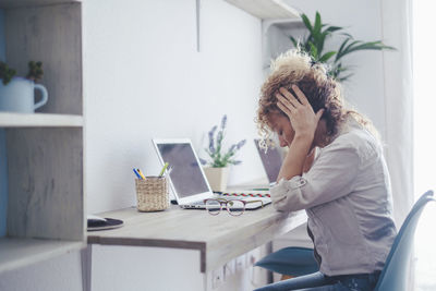 Side view of young woman using laptop at home