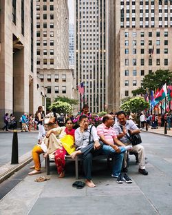 People sitting on street against buildings in city