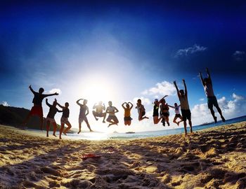 People enjoying on beach against sky during sunset