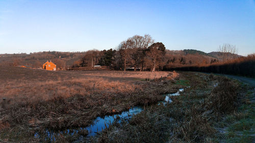 Scenic view of field and overgrown canal against clear sky