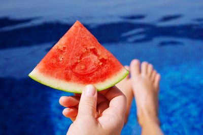 Midsection of woman holding water melon over swimming pool