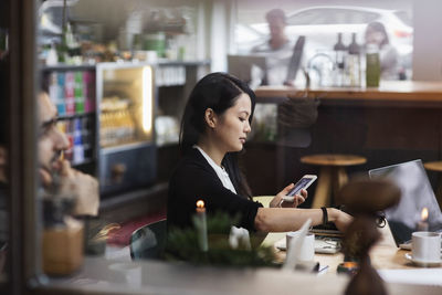 Businesswoman using phone in meeting seen through glass at creative office