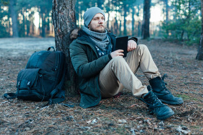 Young man looking away while sitting by tree in forest