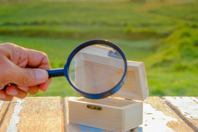 Cropped image of hand holding magnifying glass over wooden box on table