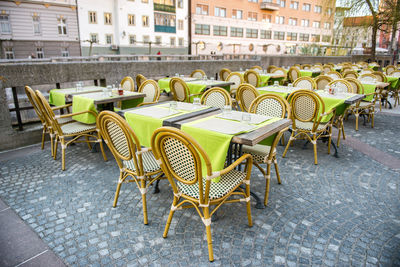 Empty chairs and tables at sidewalk cafe in city