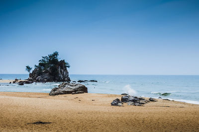 Rock formations at beach against clear blue sky