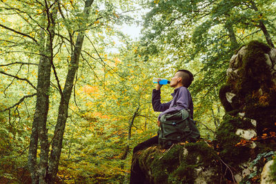 Side view of young lady with mohawk hairstyle having bottle of fresh drink hiking in autumnal park