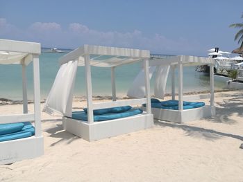 Lounge chairs by swimming pool at beach against sky