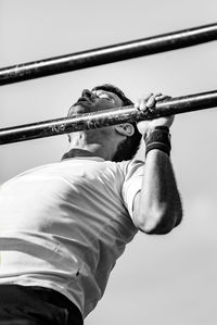 Low angle view of man doing chin-ups against sky