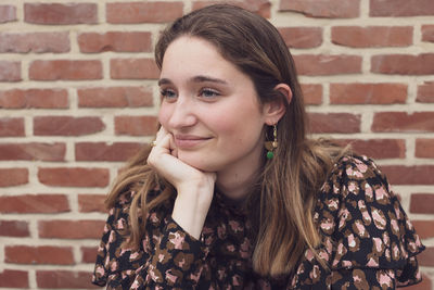 Close up shot of a beautiful brown haired teenager smiling, against a red brick 