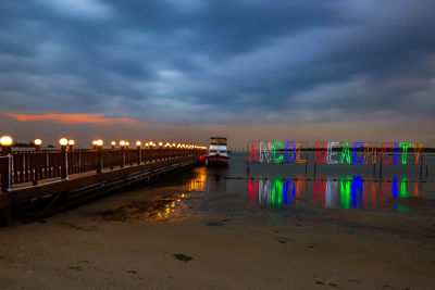 Illuminated beach by sea against sky at sunset