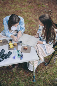 High angle view of friends looking map while sitting on chair at camp