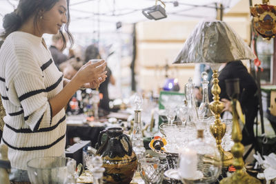 Side view of young female customer buying antique during shopping at flea market