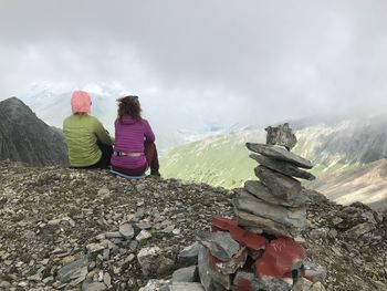 Rear view of women sitting on rocks against mountains and sky