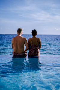 Rear view of shirtless friends in sea against sky