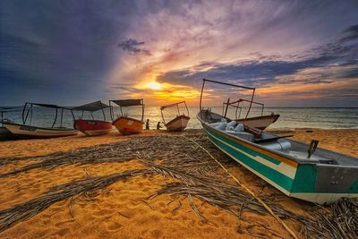 Boats moored on shore against sky during sunset