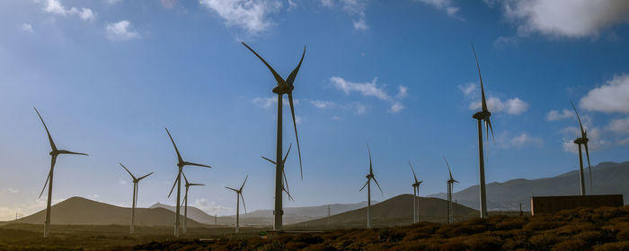 Low angle view of windmills on field against sky