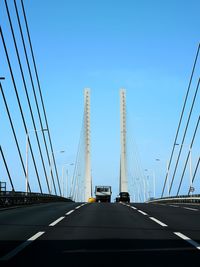 Cars on suspension bridge against sky in city