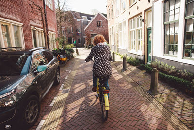 Rear view of woman riding bicycle on road amidst houses