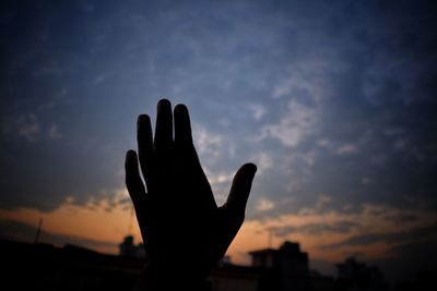 Silhouette man hand against sky at sunset