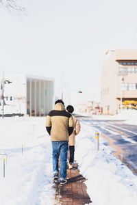 Rear view of man walking on snow covered footpath