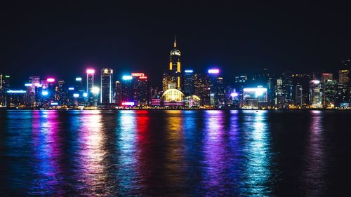 Illuminated buildings by river in city at night