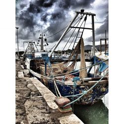 Boats in harbor against cloudy sky