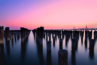 Wooden posts on pier over sea against sky during sunset