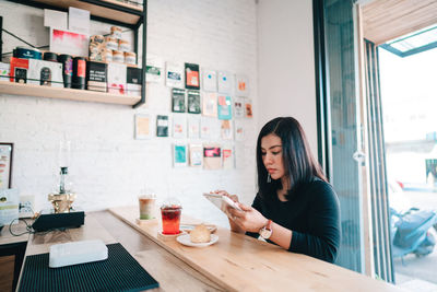 Young woman using phone while sitting on table