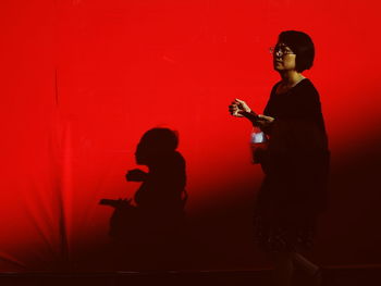 Side view of silhouette woman standing against red wall