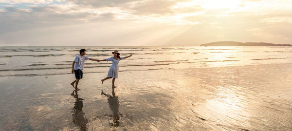 Rear view of woman walking at beach against sky during sunset