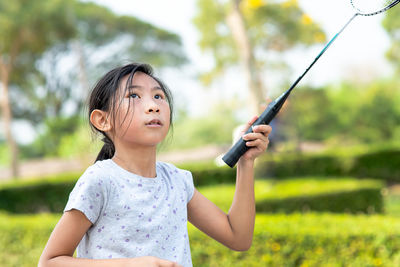 Girl holding badminton racket while standing by plants